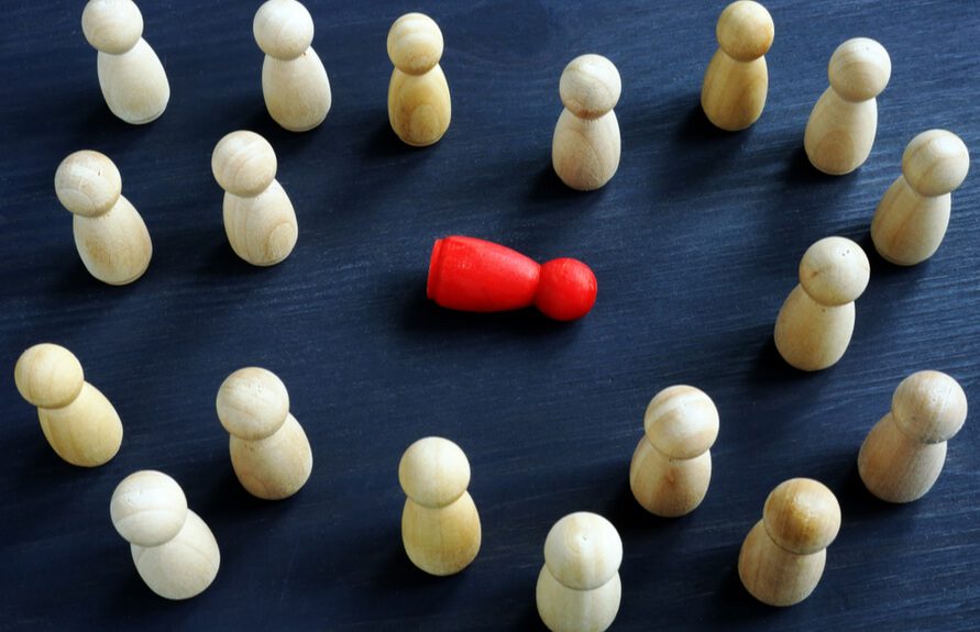 A group of wooden figurines arranged in a circular pattern, with one red figurine in the center, symbolizing individuality or standing out among the crowd.