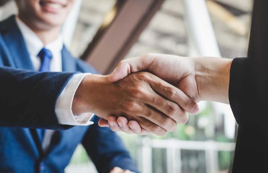 Two business professionals shaking hands in an office environment.