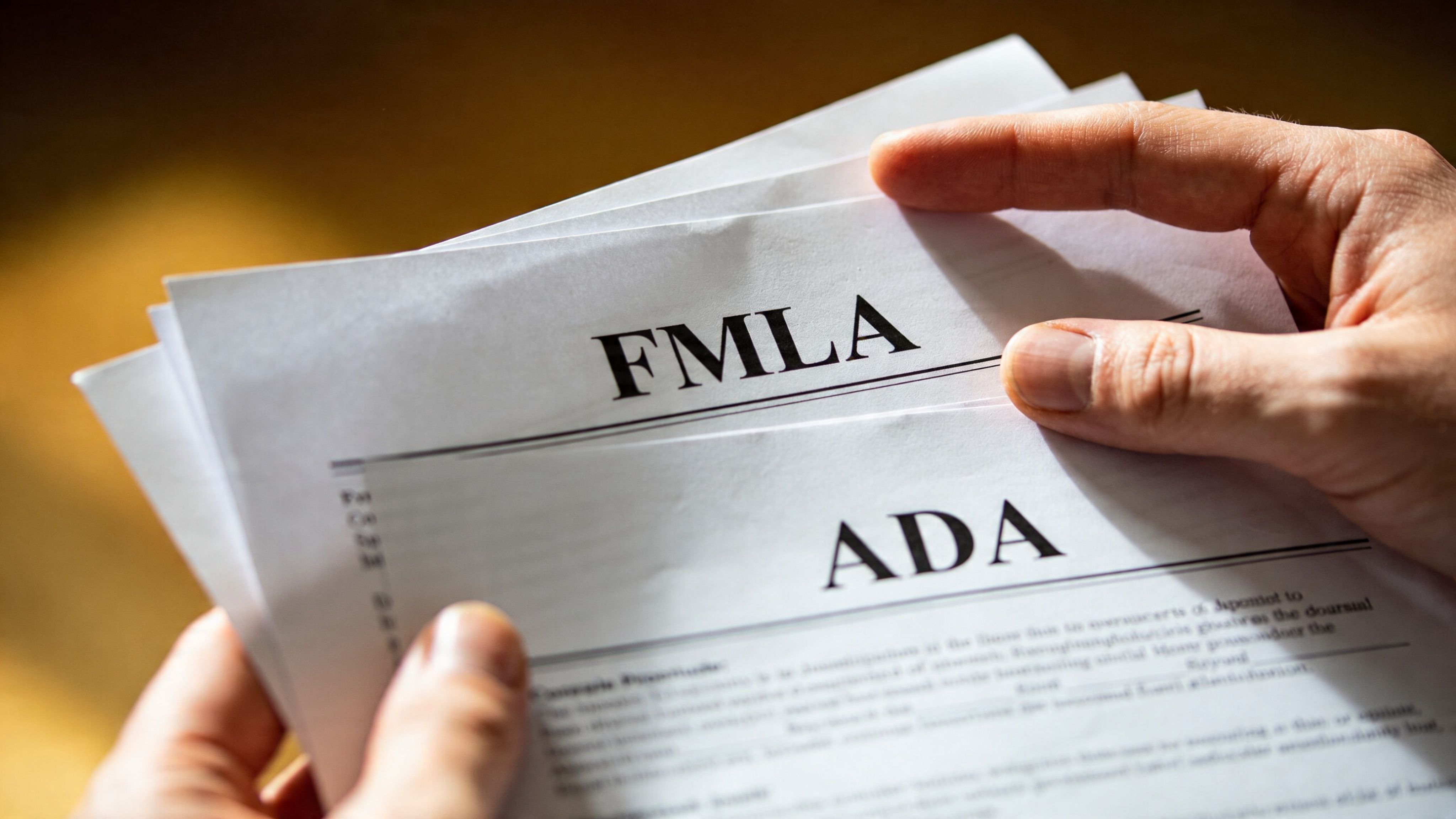 A person holding paperwork documents labeled FMLA and ADA to manage leave and disability employment protections.