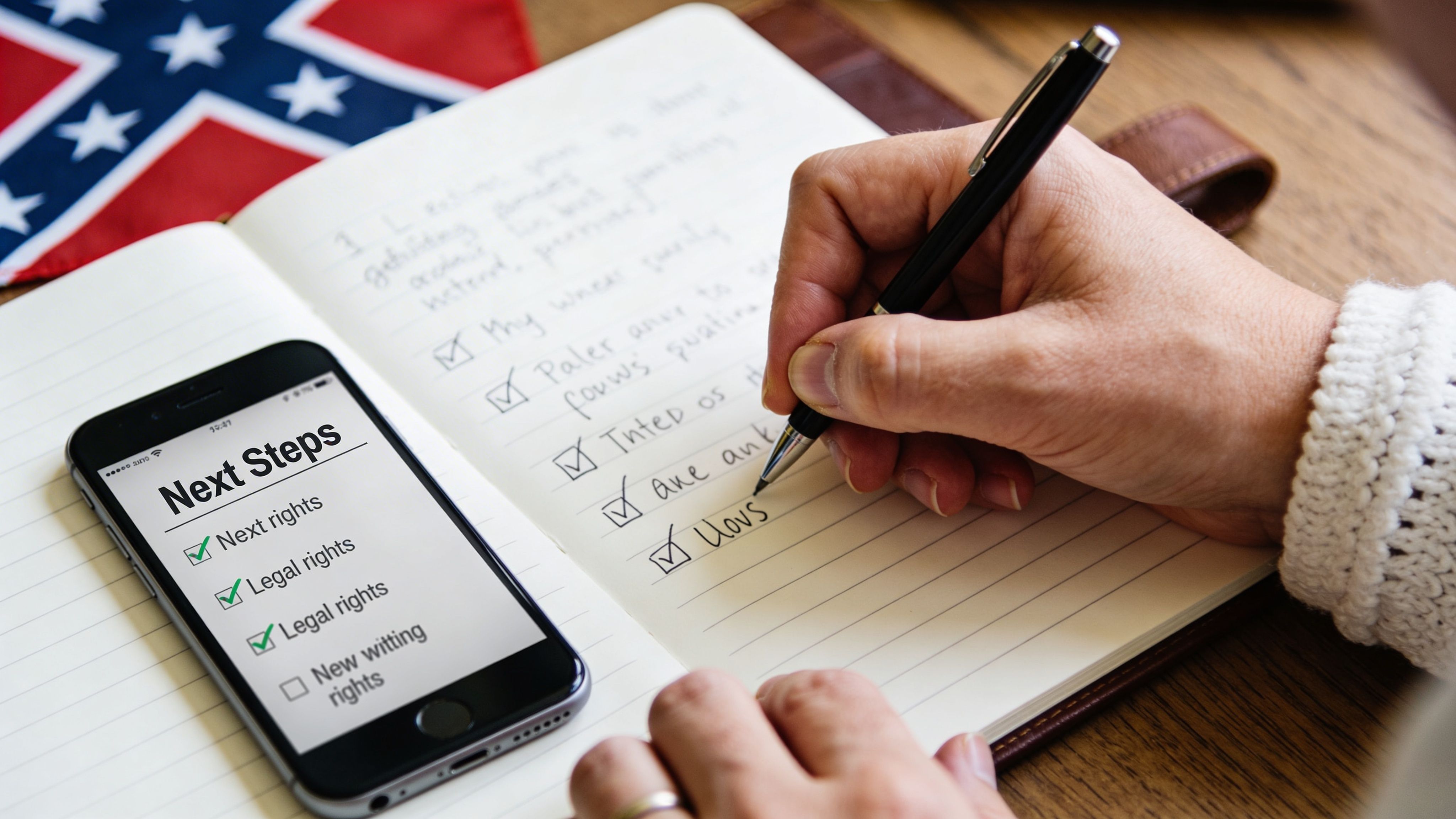 A person writes a to-do list in a notebook next to a smartphone displaying legal next steps.