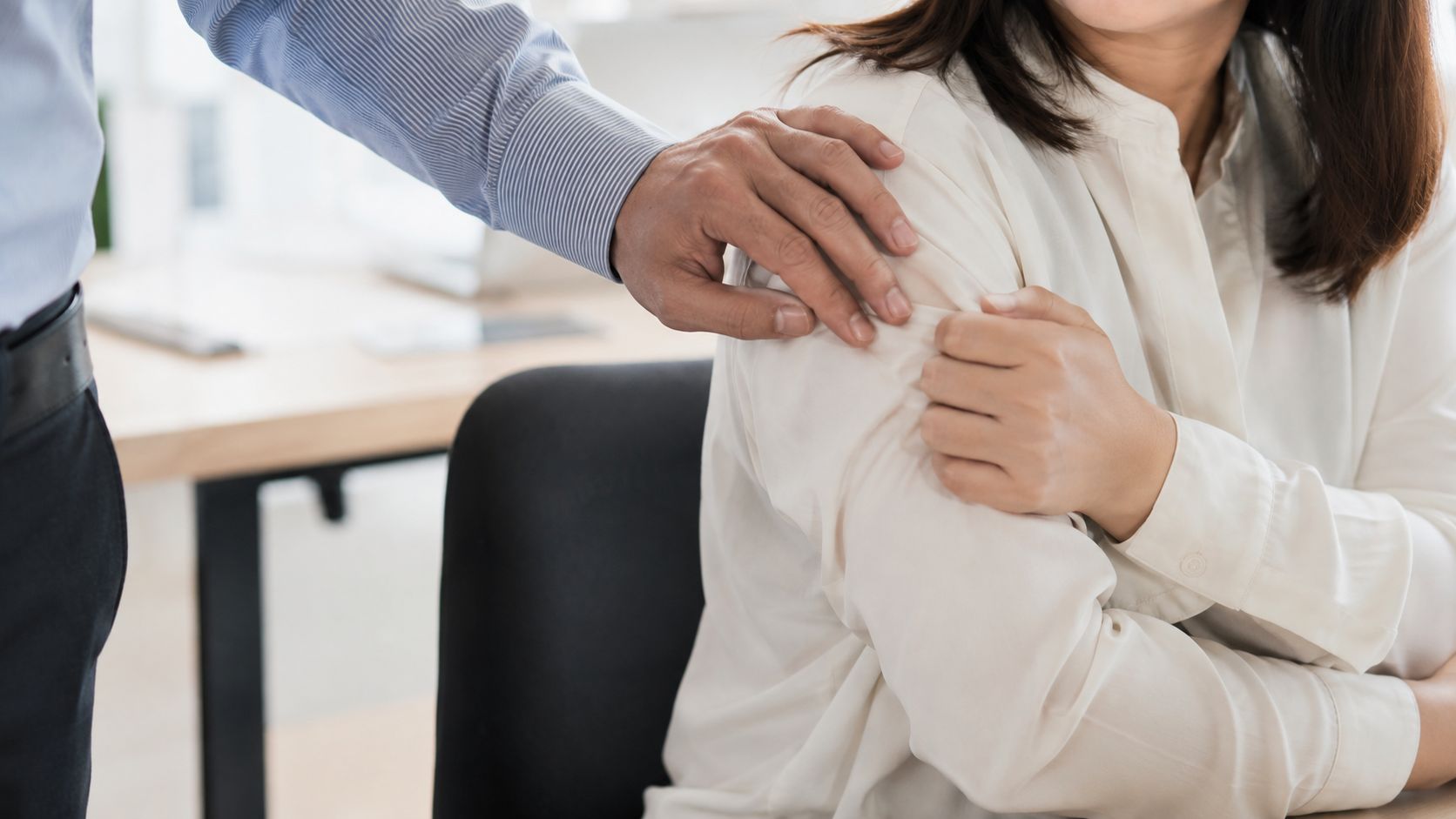 A male supervisor placing his hand on a female employee's shoulder in an office work environment.