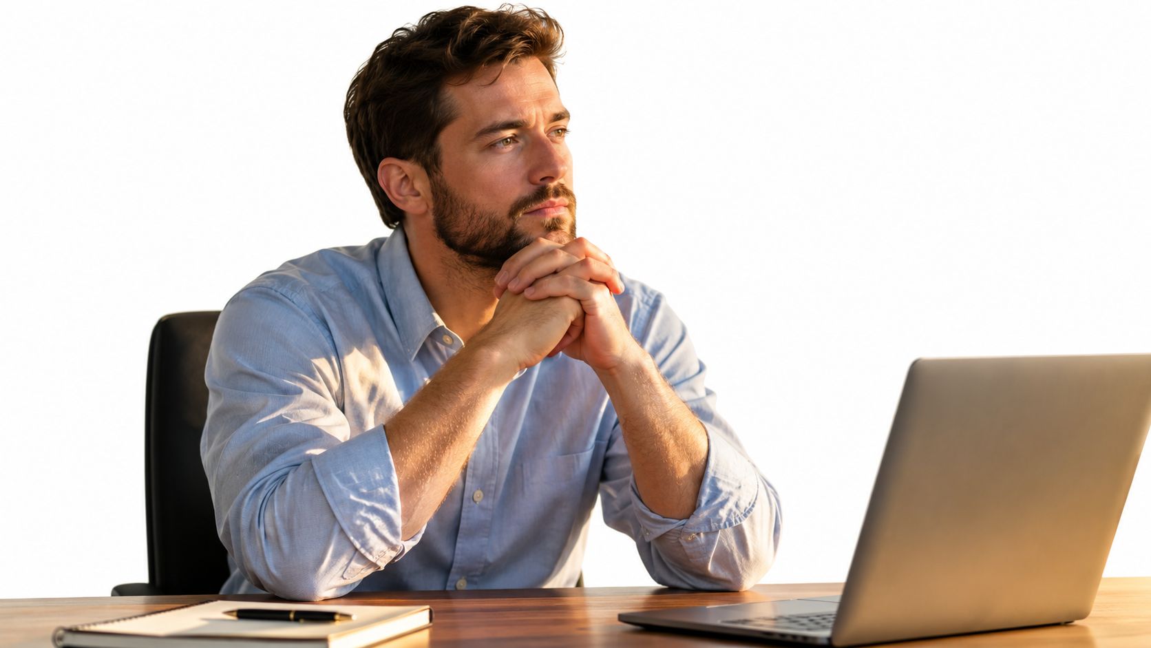 A professional man sits at a desk, looking thoughtful and concerned while using his laptop.